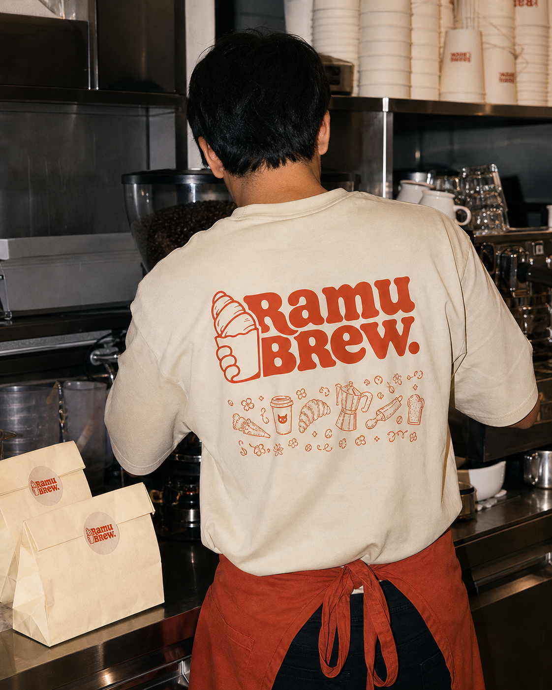 Barista Ramu Brew di balik counter dengan paper bag berstiker logo